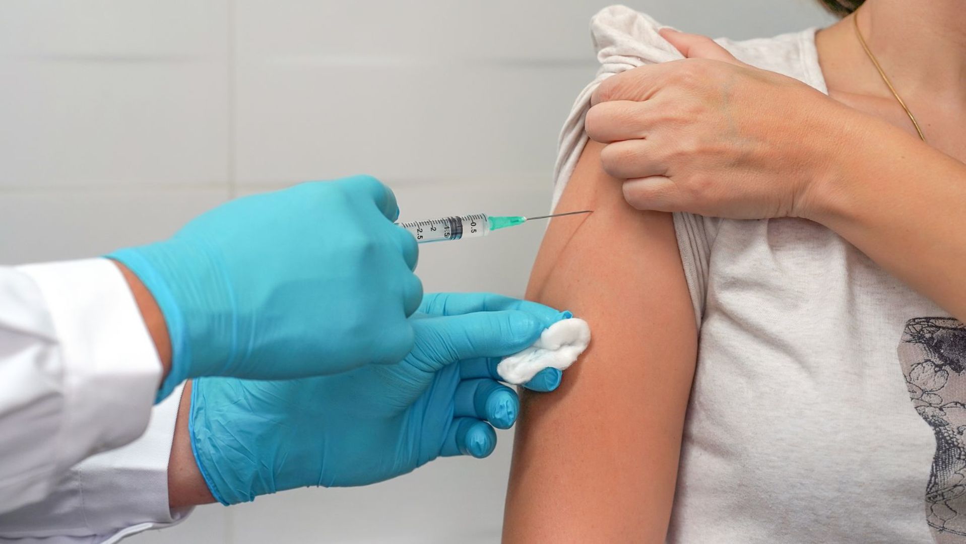 Na zdjęciu ramię osoby dorosłej odsłonięte do szczepienia oraz dłoń lekarza ze strzykawką.